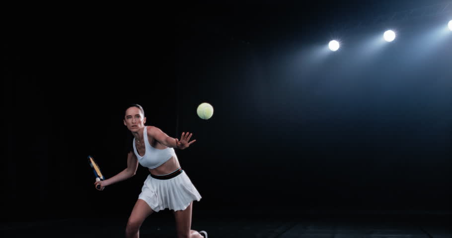 Aesthetic Shot of an Athletic Female Tennis Player with a Black Background Hitting a Low Ball Under Spotlights. Cinematic Super Slow Motion Captures a Winning Strong Forehand Shot with Smokey Effect Royalty-Free Stock Footage #1099895977