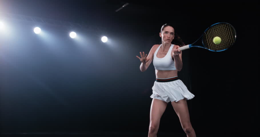 Aesthetic Shot of an Athletic Female Tennis Player with a Black Background Hitting a High Ball Under Spotlights. Arc, Cinematic Super Slow Motion Captures a Winning Strong Shot During a Championship
