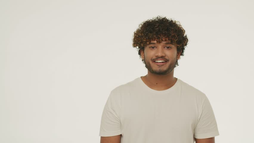 Bearded curly man pointing with finger. Excited guy celebrates triumph. Successful male model showing yes gesture on white background