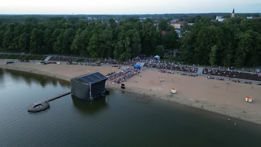 A large crowd of people at a music festival in open air. Concert nearby the lake. Festival concert at summer evening. Street music big event, Stadium on water. Open-air music festival. Estonia. 