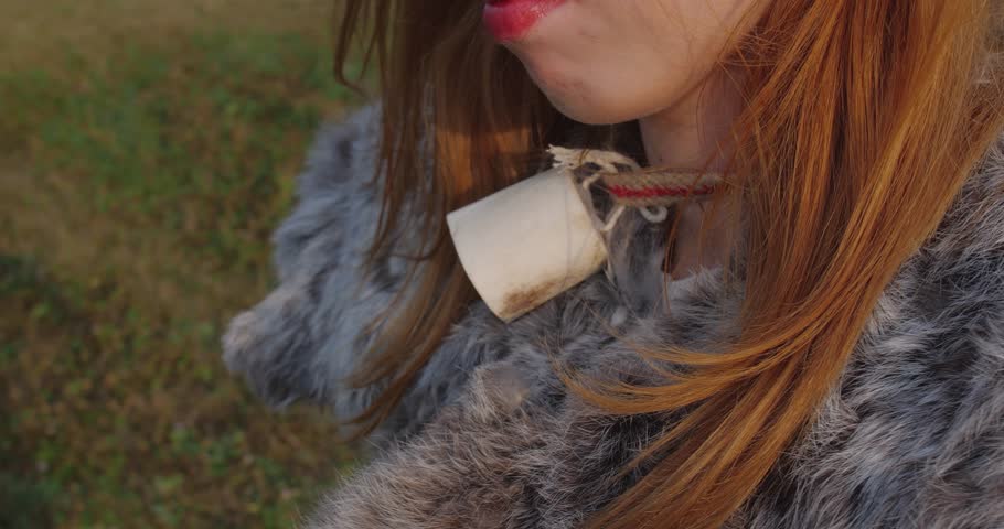 Extreme detail close up portrait, lips of blonde girl in a pagan fur costume made of animal skins standing against the background of rural landscape.