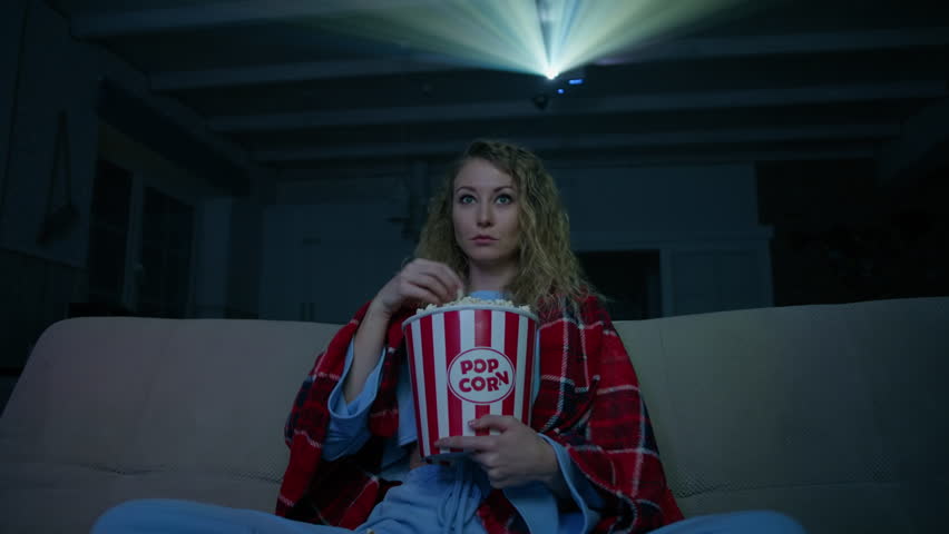 Caucasian woman watching a horror movie in her home theater. The woman spilled popcorn out of fright. High quality 4k footage Royalty-Free Stock Footage #1099903207