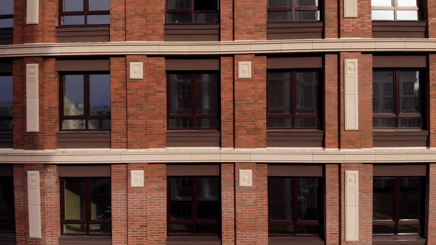 Facade of a brick multi-storey building with windows. Red brick wall. The drone takes off parallel to the building. Aerial shot Royalty-Free Stock Footage #1099906603