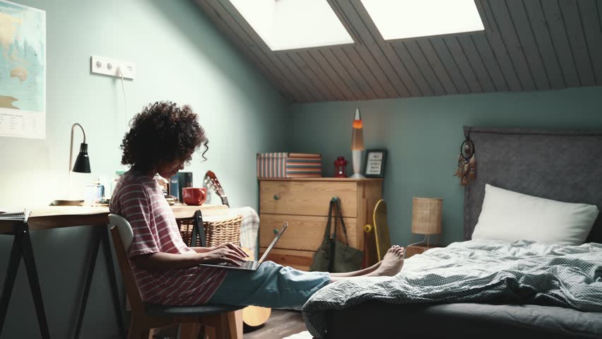 Confident curly young African girl texting on laptop in the room at home | Shutterstock HD Video #1099906877