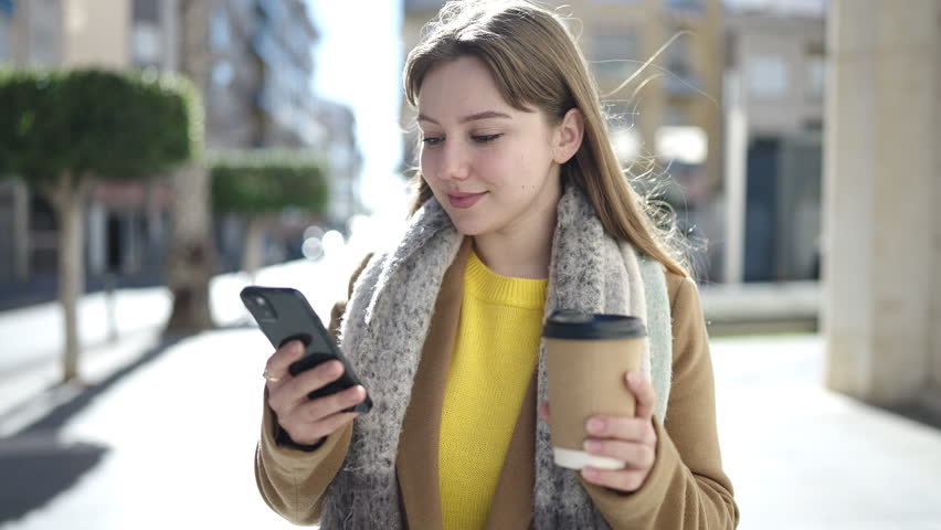Young blonde woman using smartphone drinking coffee at street | Shutterstock HD Video #1099909851
