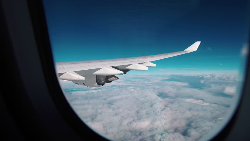 Aerial view of Cloudscape in dawn through plane window. Airplane Window View Above the Clouds. Airplane flight. Wing of an airplane flying above the clouds. 