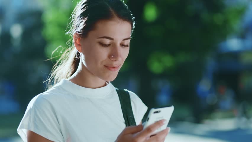 happy hispanic latin goes in city urban street using smartphone at sunny weather park threes background. Smiling beautiful female using mobile phone. Royalty-Free Stock Footage #1099920955