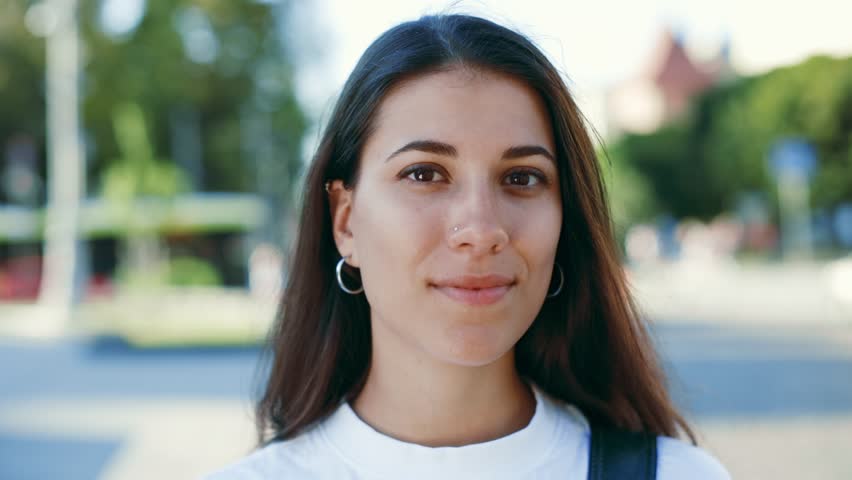 Portrait of a beautiful dark haired hispanic woman smiling look at camera standing in the urban city centre background at sunny warm weather wearing casual white t-shirt. Happy Young Woman Enjoys Life | Shutterstock HD Video #1099920965