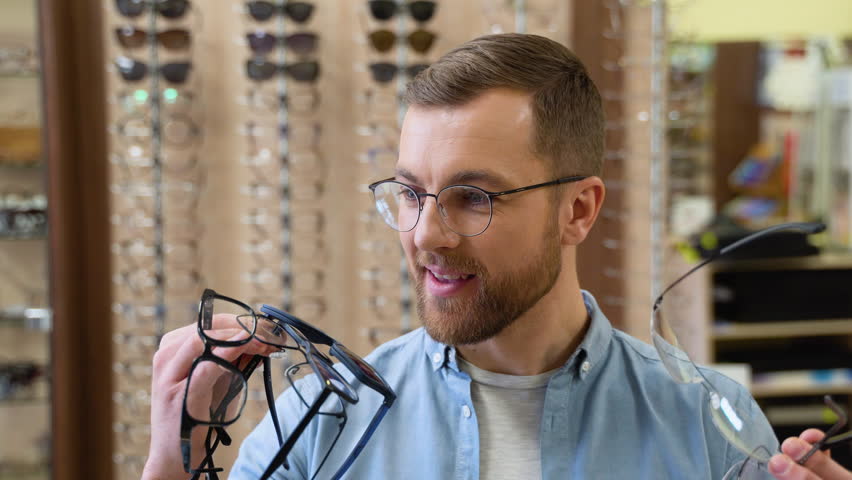 Excited surprised man holds many new glasses in his hands at optical shop. Choosing glasses concept Royalty-Free Stock Footage #1099923941
