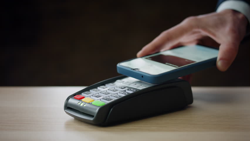 Cashless payment using smartphone on modern bank terminal indoors close up. Unknown person making purchase with contactless nfc technology. Man hand holding telephone for pay pass transaction.  | Shutterstock HD Video #1099925209