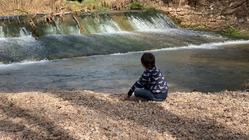 Boy playing with stones on the river bank | Shutterstock HD Video #1099927305