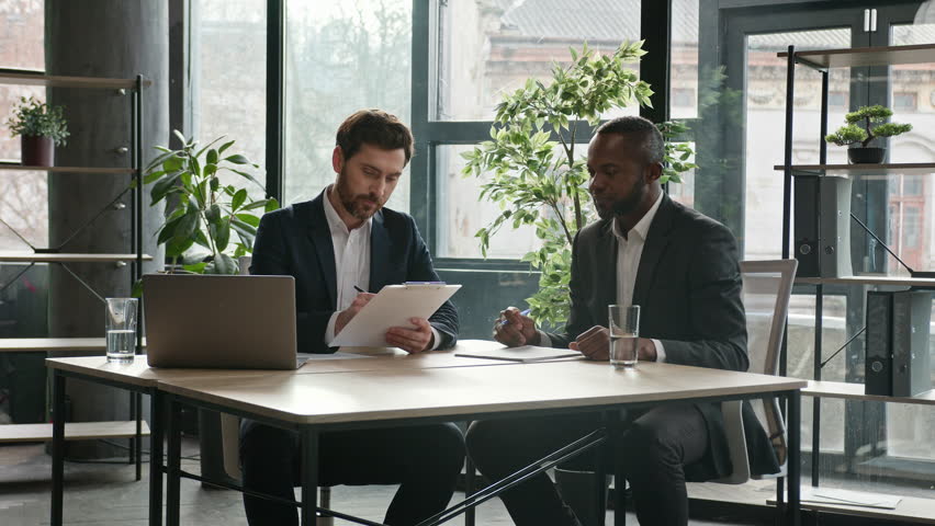 Multiethnic Caucasian and African American business people diverse men two male partners at office desk sign document shake hands signing corporate paper contract handshaking successful partnership Royalty-Free Stock Footage #1099927903