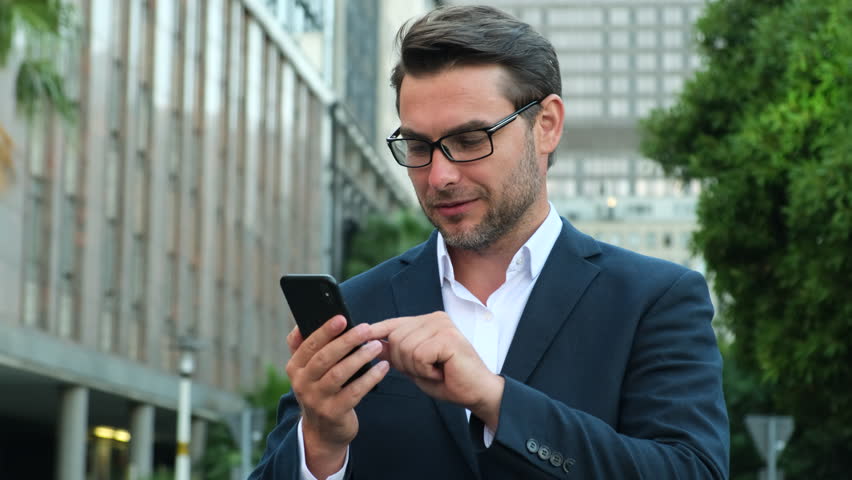 Male millennial professional holding modern smartphone texting message. Young businessman using helpful mobile apps for business time management organization concept. | Shutterstock HD Video #1099928587