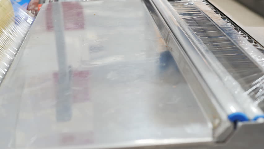 A grocery store clerk packed thinly sliced sausages into a styrofoam tray and wrapped the stretch film using a retail food wrapper. | Shutterstock HD Video #1099929205