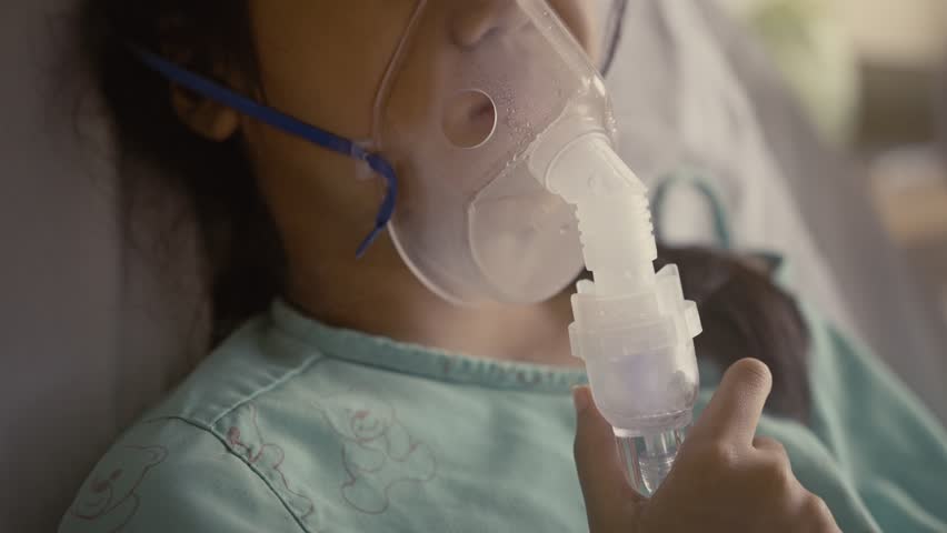 Asian girl having an oxygen mask and breathing through a nebulizer at the hospital. | Shutterstock HD Video #1099931369