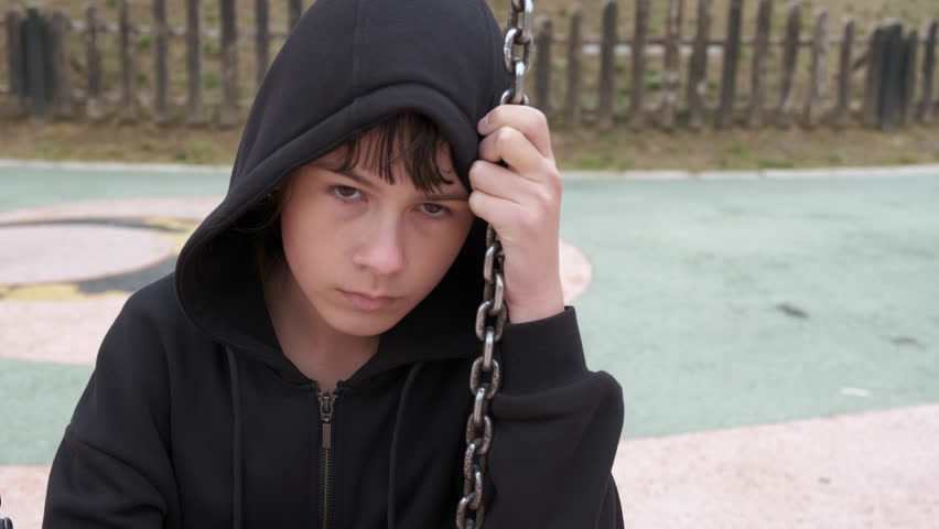 Teen spends time alone on playground. An upset teen girl spend her time on swing on empty playground. | Shutterstock HD Video #1099931819