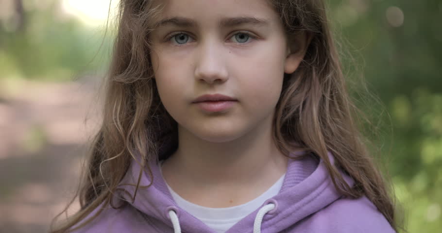 Portrait Child Girl Looking at Camera Standing on Street in City on Summer Day. Sad Thinking Curiosity Teenager Looking at Camera Closeup Outdoors. Human Face Eyes Serious Contemplative Child. | Shutterstock HD Video #1099934295