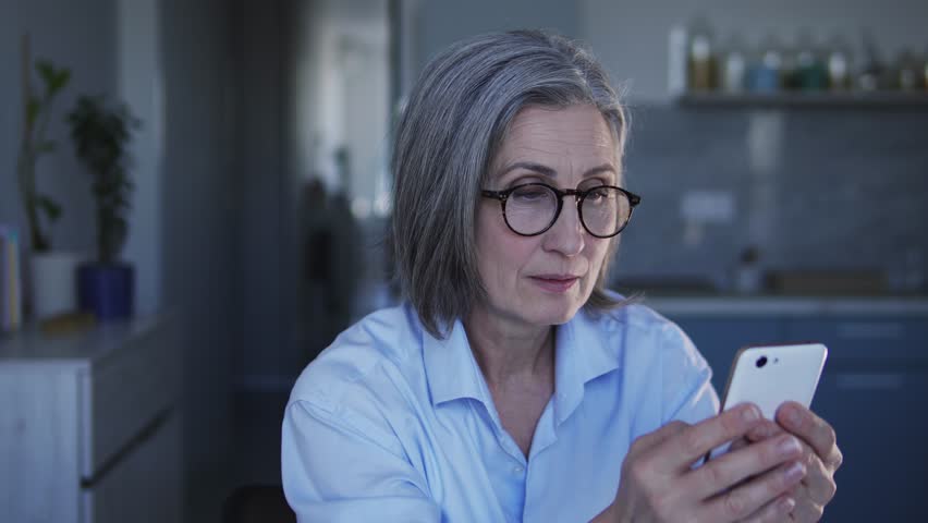 Serious woman boss with gray hair checking report of her employees on smartphone and going crazy through mistakes in work and incompetent execution of assignments and duties | Shutterstock HD Video #1099937871