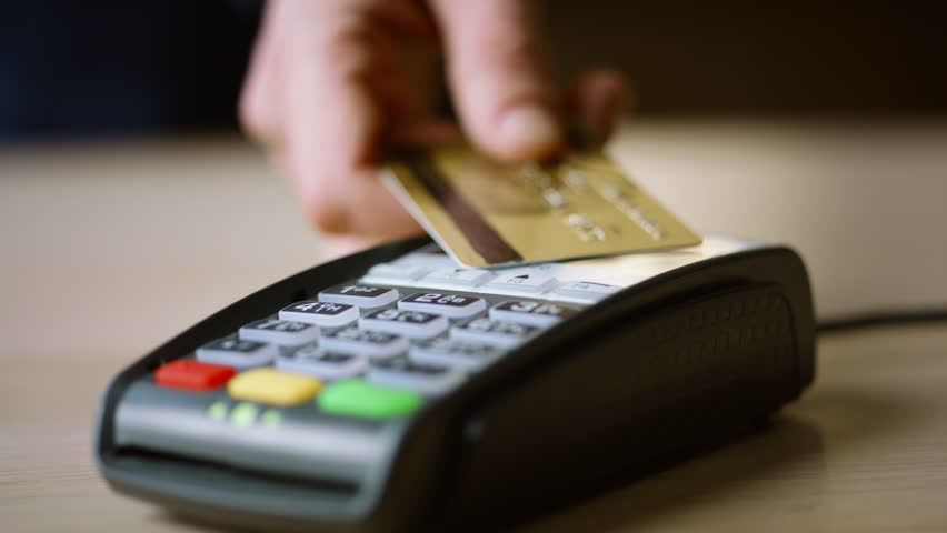 Contactless credit card payment on bank terminal close up. Man hand paying for purchase with NFC technology touching pos reader. Unknown customer using wireless money transaction. Cashless operation.
