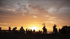 Time lapse of silhouettes of a crowd at sunset on the beach fade out. Time lapse of the silhouette of unrecognizable people sitting on a summer sunset on the beach.