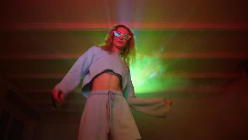 Happy young woman enjoys watching a concert at home. Caucasian woman with curly hair is dancing on the couch. High quality 4k footage