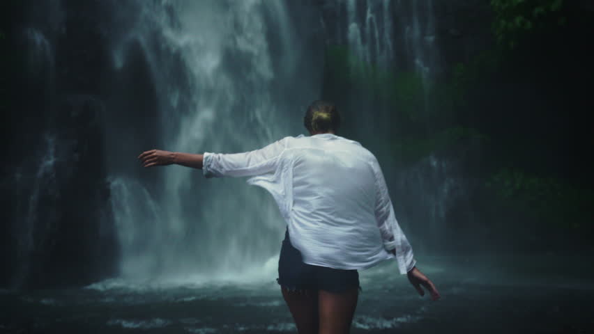 Back of woman woman in straw hat enjoying breathtaking high waterfall Sekumpul with rain in Bali rainforest. Great wild nature of Indonesia Royalty-Free Stock Footage #1099947803
