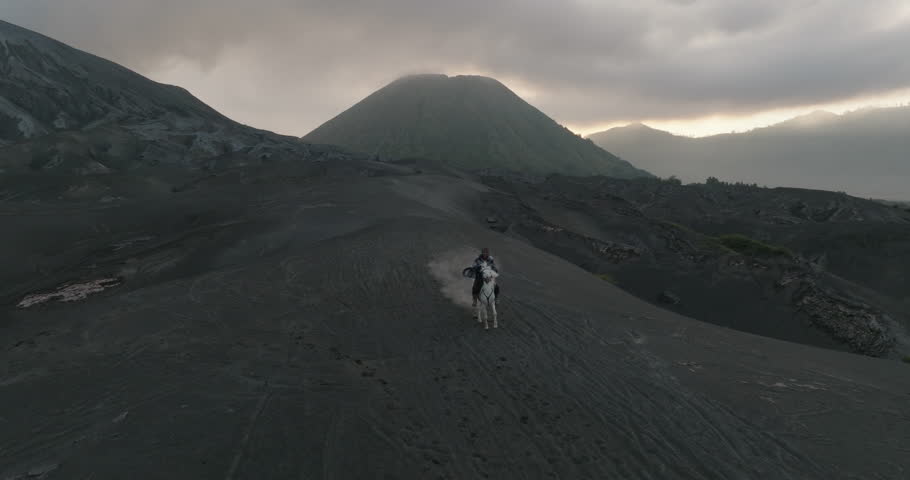 Aerial Backward Shot Of Tourist Riding Horse On Volcanic Landscape Under Clouds In Sky During Sunset - Java, Indonesia