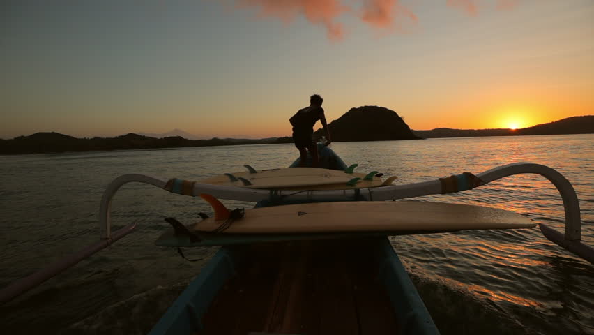 Slow Motion Shot Of Silhouette Of Man Standing In Outrigger Canoe Moving On Sea During Sunset - Lombok, Indonesia