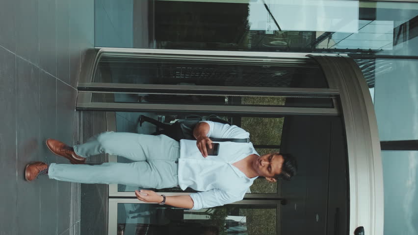 VERTICAL VIDEO: Young businessman leaving the business center with smartphone | Shutterstock HD Video #1099959573