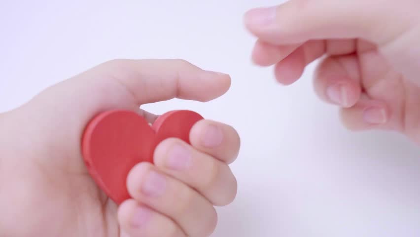 Close up of mother hand giving to her child red heart on white pastel background. Family relationship, family wellness love concept. Mother gives to her kid red heart | Shutterstock HD Video #1099963645