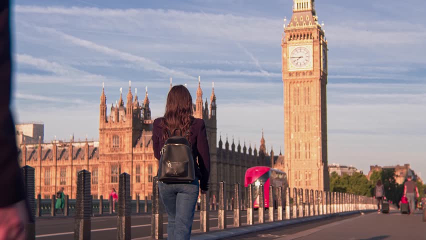 Tracking shot of young woman walking on Westminster Bridge London with Big Ben view. Stylish trendy tourist woman having a walk on Westminster Bridge on a morning sunny day
