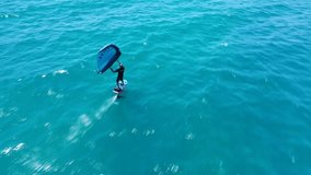 Aerial drone video of fit athlete practise hydro foil wing surfing in tropical exotic bay