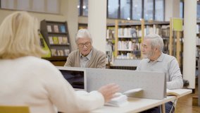 Teacher talking with senior people studying in library. Cheerful elderly men and woman sitting at desk, reading books, using laptops, devoting time to hobby together. Education, retirement concept - Powered by Shutterstock - Get 15% off with code: PIKWIZARD15