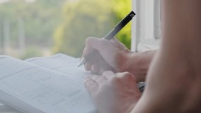 Close up video of woman writing in her planner agenda in front of window