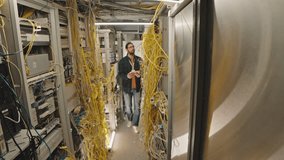 Full length shot of Caucasian male server room manager in streetwear walking along row with network panels and controlling their work on digital tablet - Powered by Shutterstock - Get 15% off with code: PIKWIZARD15