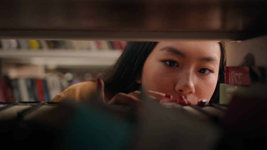 Close-up young asian woman browsing shelves books concentrated female student looking for necessary book to read on bookshelf searching right textbook to prepare for exam search literature in library Royalty-Free Stock Footage #1099973855