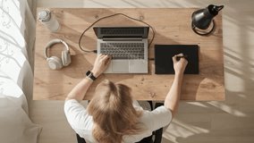 Top down view, freelancer woman in white t-shirt sits down at her desk and starts drawing on graphics tablet at home. Young woman stretching, close laptop and go away. - Powered by Shutterstock - Get 15% off with code: PIKWIZARD15