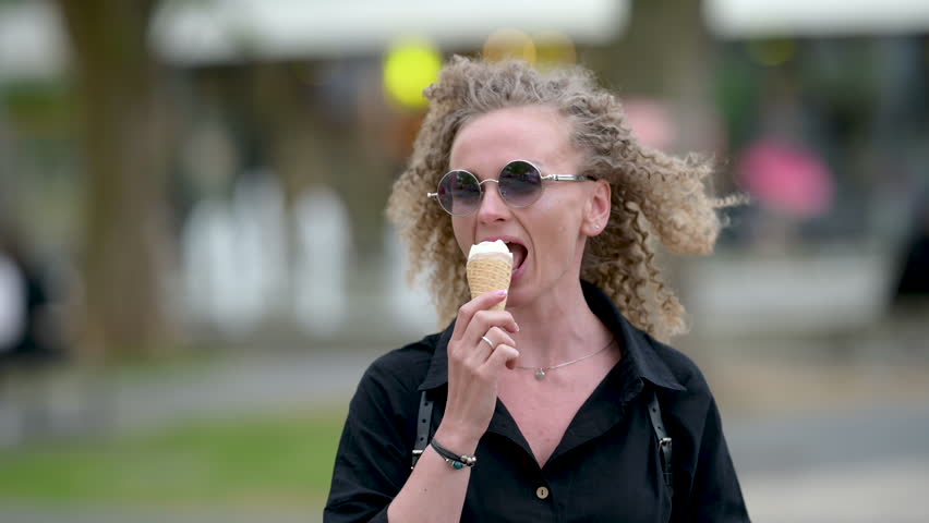 Girl with curly hair smiling while eating a fresh ice cream cone outdoors in the street.	