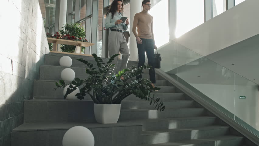 Low angle view of business colleagues walking down the stairs in modern office and discussing working moments | Shutterstock HD Video #1099980517