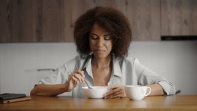 Curly-haired woman enjoying healthy breakfast in the kitchen, eating oatmeal - Powered by Shutterstock - Get 15% off with code: PIKWIZARD15