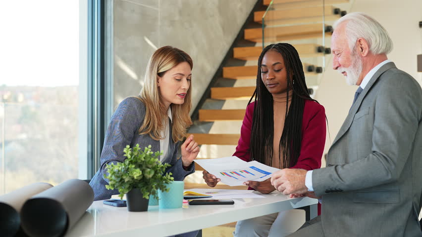 Team of professionals working together reviewing few finance documents with charts and graphs in business meeting. Senior businessman is happy to hearing of new ideas from younger coworkers.  | Shutterstock HD Video #1099981965