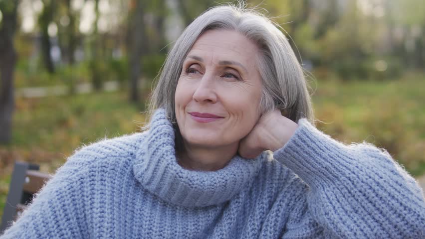 Happy inspired lady in her 60s sitting on bench in garden of her Vacation home, smiling and enjoying beautiful landscapes and fresh air, escape from bustled city, harmony | Shutterstock HD Video #1099982083