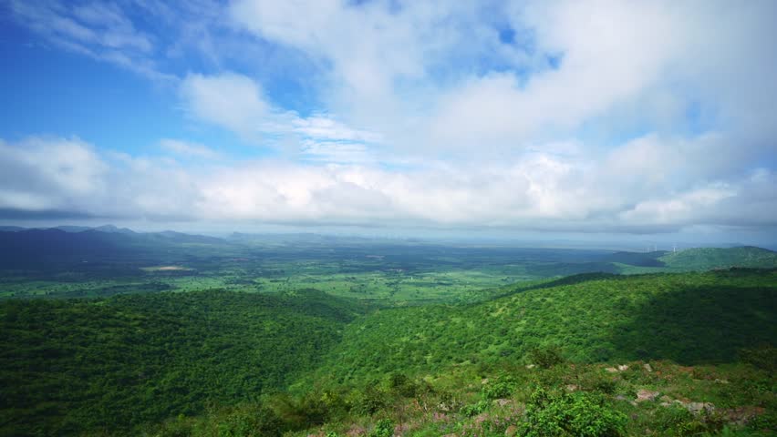 An horizontal view of calm blue sky and hills filled with green plants and trees