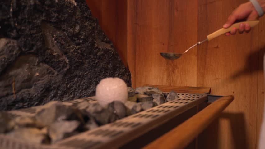 A female hand pouring water into hot stones with salt brick in a sauna room Royalty-Free Stock Footage #1099992609