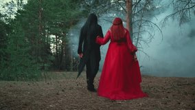 Goth man vampire in black tailcoat walking with gothic woman holding hand. fantasy couple two person back rear view Red dress. Fog forest tree summer green nature. Guy with long dark hair wig video 4k