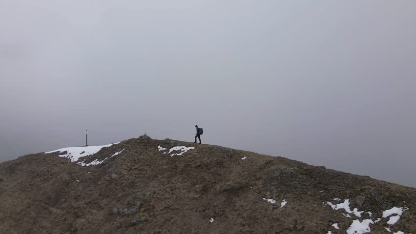 An HD of a hiker walking on the top of the mountain while snowing