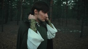 Portrait fantasy male elf prince. man thief puts hood on head hides face. Dark gothic dense forest. Mystical evil fairy guy assassin. Creative old style clothes cloak green cape. Fashion model posing - Powered by Shutterstock - Get 15% off with code: PIKWIZARD15
