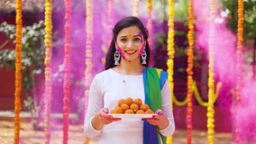 Happy smiling girl with coloured face holding sweet or laddu by looking at camera on flower decorated background - concept of holi festival, happiness and joyful. - Powered by Shutterstock - Get 15% off with code: PIKWIZARD15