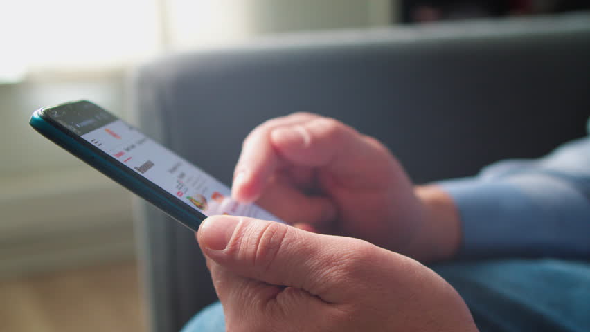 Man looks at a menu on a smartphone and chooses a delivery burger. Man searches for a varied menu and burgers on a smartphone app before ordering food online. browsing mobile site on smartphone.