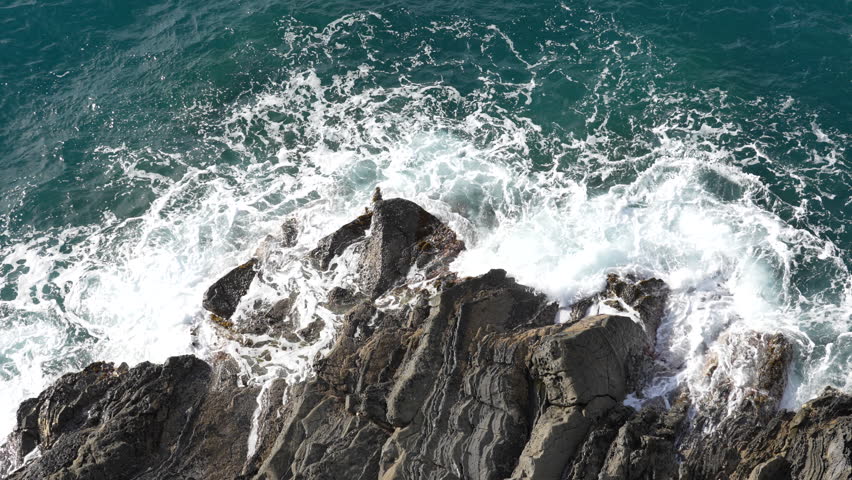 Top down aerial view of ocean waves crashing onto a rocky shoreline.